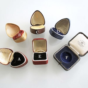 Puede incluir: Un surtido de joyeros vintage abiertos de varias formas y colores. Las cajas incluyen ejemplos dorados, rojos, marrones y azules. Los interiores están forrados con terciopelo y satén en colores como el rojo, el negro y el azul.