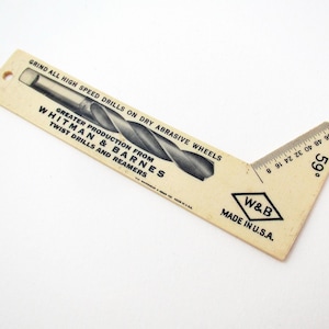 May include: A beige L-shaped Whitman & Barnes drill point gauge with black text reading GRIND ALL HIGH SPEED DRILLS ON DRY ABRASIVE WHEELS, GREATER PRODUCTION FROM TWIST DRILLS AND REAMERS, W&B, MADE IN U.S.A., and a 59 degree angle marking.