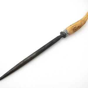 May include: A sharpening steel featuring a long, tapered, dark grey metal rod and a curved, textured tan handle made of natural material. A silver-coloured metal ferrule with vertical ridges connects the handle to the sharpening rod.