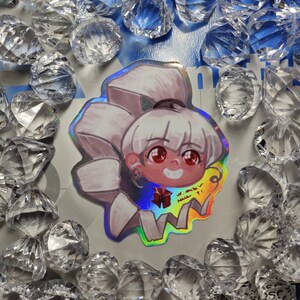 Può includere: Un adesivo olografico con un personaggio dei cartoni animati con capelli bianchi, occhi rossi e un fiocco rosso. Il personaggio sorride e ha un fumetto che dice "Sono così felice!"