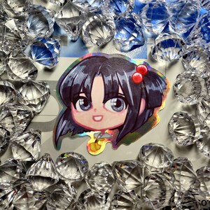 May include: A holographic sticker featuring a cartoon character with dark blue hair, wearing a red bow with white polka dots. The character has a light pink complexion and is smiling. The sticker has a shiny, iridescent finish.