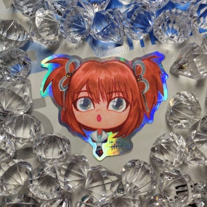 May include: A holographic sticker featuring a cartoon illustration of a girl with red hair, wearing a white shirt and a blue skirt. She has pigtails with blue ribbons and a surprised expression.