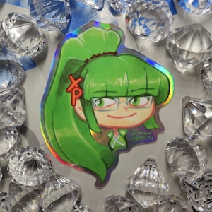 May include: A holographic sticker featuring a cartoon character with green hair, wearing glasses and a green and white outfit. The character has a red "XP" on their hair.