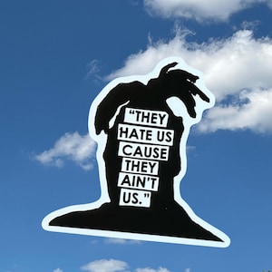 May include: A black die-cut sticker featuring the silhouette of a person with dreadlocks. The center of the silhouette contains the white text "THEY HATE US CAUSE THEY AIN'T US." in a bold, block-letter font, arranged in five stacked lines.