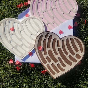 K&ouml;nnte beinhalten: Drei herzf&ouml;rmige Karten in Wei&szlig;, Rosa und Braun, jede mit einem einzigartigen Ausschnitt, werden auf gr&uuml;nem Gras pr&auml;sentiert. Rote herzf&ouml;rmige Konfetti sind um die Karten verstreut, was auf ein romantisches Thema hindeutet.