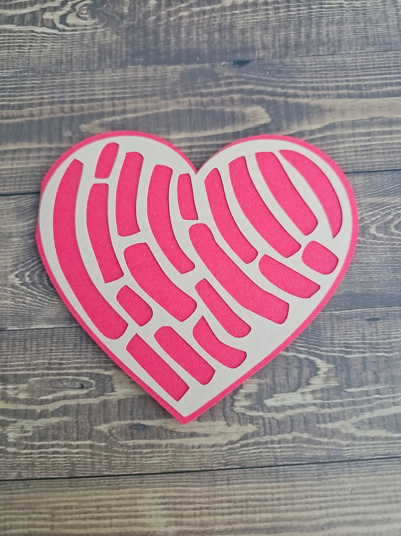K&ouml;nnte beinhalten: Ein herzf&ouml;rmiger Papierauschnitt in leuchtendem Pink, mit einem einzigartigen Muster aus gebogenen Linien und Formen. Der Ausschnitt ist auf einer hellbraunen R&uuml;ckseite angeordnet, was einen Kontrast erzeugt. Der Hintergrund ist eine Holzoberfl&auml;che.