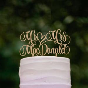 May include: A three-tiered ombre wedding cake with purple frosting. The cake is decorated with a wooden cake topper that says "Mr & Mrs Mac Donald".