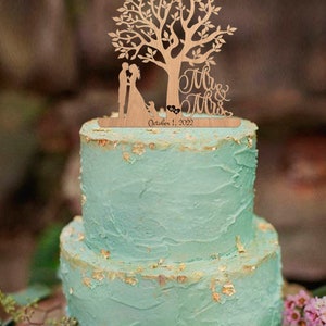 May include: A wooden wedding cake topper featuring a couple standing under a tree with a dog at their feet. The topper says "Mr. & Mrs." and "October 1, 2022".