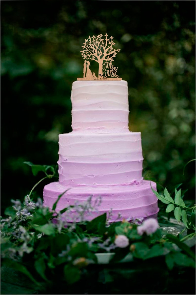 May include: A three-tier ombre wedding cake with purple frosting. The cake is decorated with a wooden topper featuring a couple standing under a tree with the words "Mr. & Mrs." and the date "October 1, 2022".