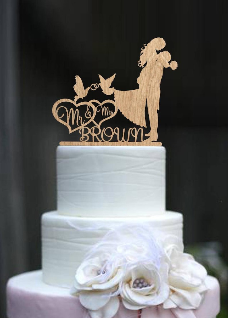 K&ouml;nnte beinhalten: Holz-Tortenaufsatz f&uuml;r Hochzeit mit einem sich umarmenden Paar, zwei V&ouml;geln mit einem Ring und dem Text "Mr & Mrs Brown".