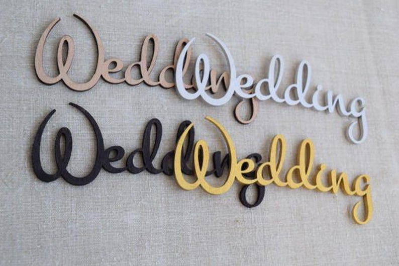 K&ouml;nnte beinhalten: Vier Holzschilder mit der Aufschrift "Wedding" in verschiedenen Farben: Naturholz, Wei&szlig;, Schwarz und Gold.