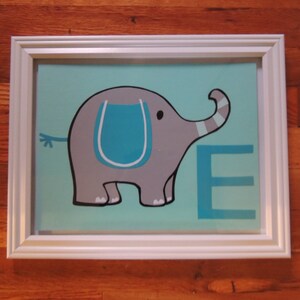 May include: A framed artwork featuring a gray cartoon elephant with a blue accent on a light blue background. The letter "E" is displayed in blue. The artwork is encased in a white frame.