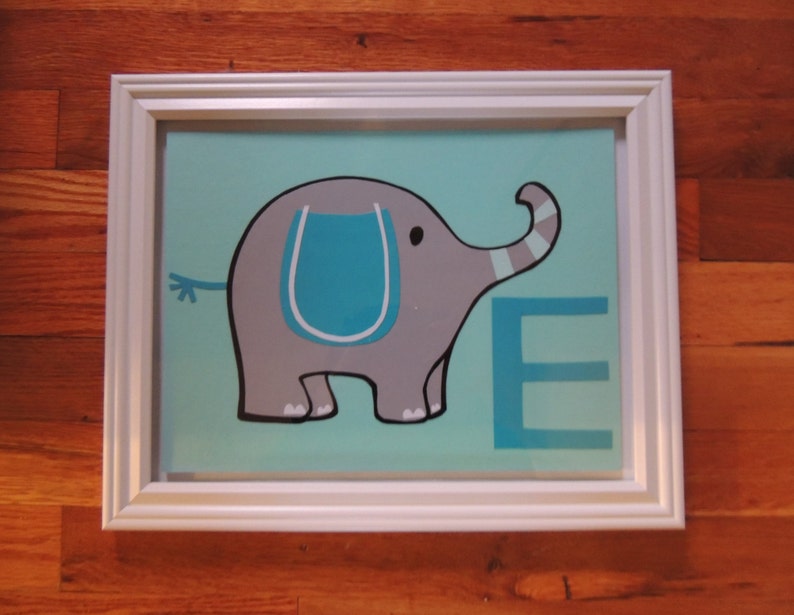 May include: A framed artwork featuring a gray cartoon elephant with a blue accent on a light blue background. The letter "E" is displayed in blue. The artwork is encased in a white frame.
