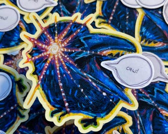 May include: A blue and yellow sticker with a detailed illustration of a crow with a starburst behind it. The sticker has a speech bubble that says "caw!"