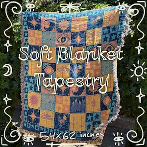 May include: A soft tapestry blanket with a celestial design. The blanket features a patchwork pattern with squares of blue, yellow, and pink, adorned with moons, stars, and eyes. It measures 137x157 cm.