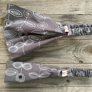 Könnte beinhalten: Zwei graue Stirnbänder mit einem weißen Blumenmuster. Die Stirnbänder haben ein kleines Etikett mit dem Text "La La" darauf.