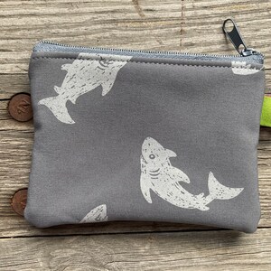 Puede incluir: Una bolsa gris con cremallera con estampado de tiburón blanco. La bolsa tiene una etiqueta verde con el texto "Lia's" en ella.