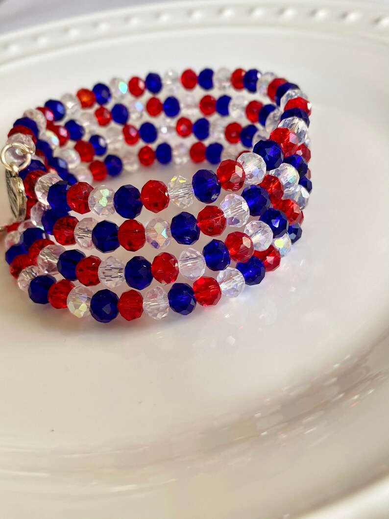 Pu&ograve; includere: Un braccialetto multifilo realizzato con perline rosse, bianche e blu. Il braccialetto &egrave; realizzato con piccole perline sfaccettate ed &egrave; avvolto a spirale.
