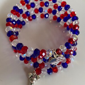 Pu&ograve; includere: Un braccialetto di perline rosso, bianco e blu con un ciondolo d'argento a forma di chiave con le orecchie di Topolino e un ciondolo d'argento a forma di cuore con un design di bandiera americana.