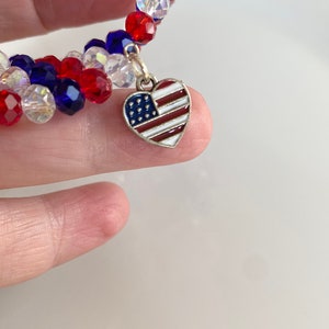 Pu&ograve; includere: Un braccialetto di perline rosso, bianco e blu con un ciondolo a forma di cuore argentato con un design di bandiera americana.