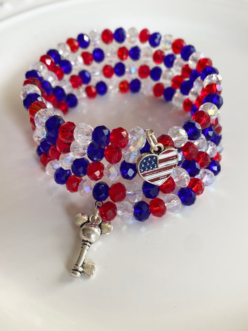 Pu&ograve; includere: Un braccialetto di perline rosso, bianco e blu con un ciondolo a forma di cuore con la bandiera americana e un ciondolo a forma di chiave.