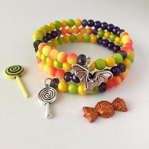 May include: A multi-layered bracelet with yellow, orange, and green beads, accented with purple beads. The bracelet has a silver bat charm and two silver lollipop charms.