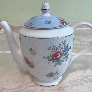 Puede incluir: Tetera de cerámica blanca con diseño floral. La tetera tiene una tapa azul claro con diseño floral y ribete dorado. El cuerpo es blanco con lunares azules y detalles florales rojos y azules. Un complemento encantador para cualquier juego de té.