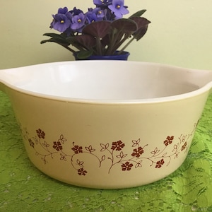 Puede incluir: Un tazón mezclador grande de color crema con un diseño floral marrón. El tazón tiene una base ancha y redondeada y dos asas a los lados.