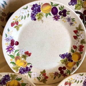 Op de afbeelding: Een wit keramiek dinerbord met een rand versierd met een kleurrijk bloemenpatroon met druiven, pruimen, peren, aardbeien en kersen.