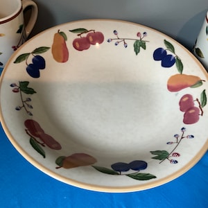 May include: A white ceramic bowl with a rim of beige. The bowl has a fruit and floral design in shades of red, green, blue, and yellow.