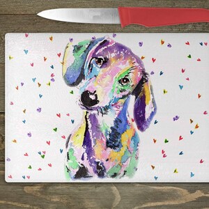 May include: A colorful watercolor painting of a dachshund dog with a white background and scattered hearts in various colors. The dog is looking to the left of the image.