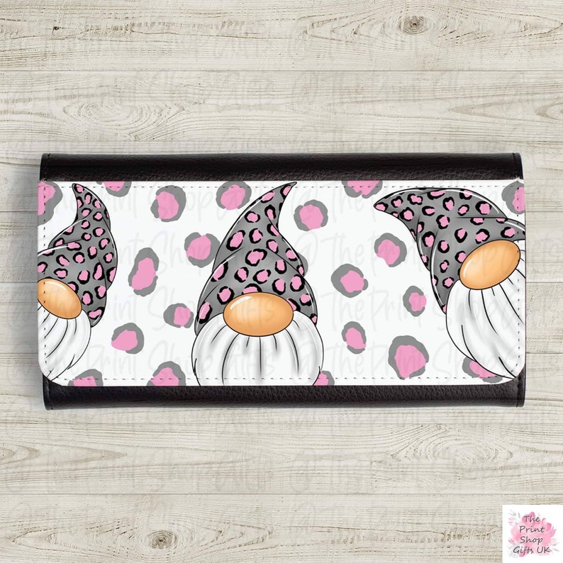 Op de afbeelding: Een zwarte leren portemonnee met een witte achtergrond en een roze en zwart luipaardprint ontwerp. Het ontwerp bevat drie gnomes met roze en zwarte hoeden.