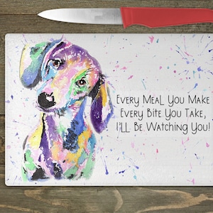 May include: A colorful watercolor painting of a dachshund dog on a white cutting board with the text "Every meal you make every bite you take, I'll be watching you!"