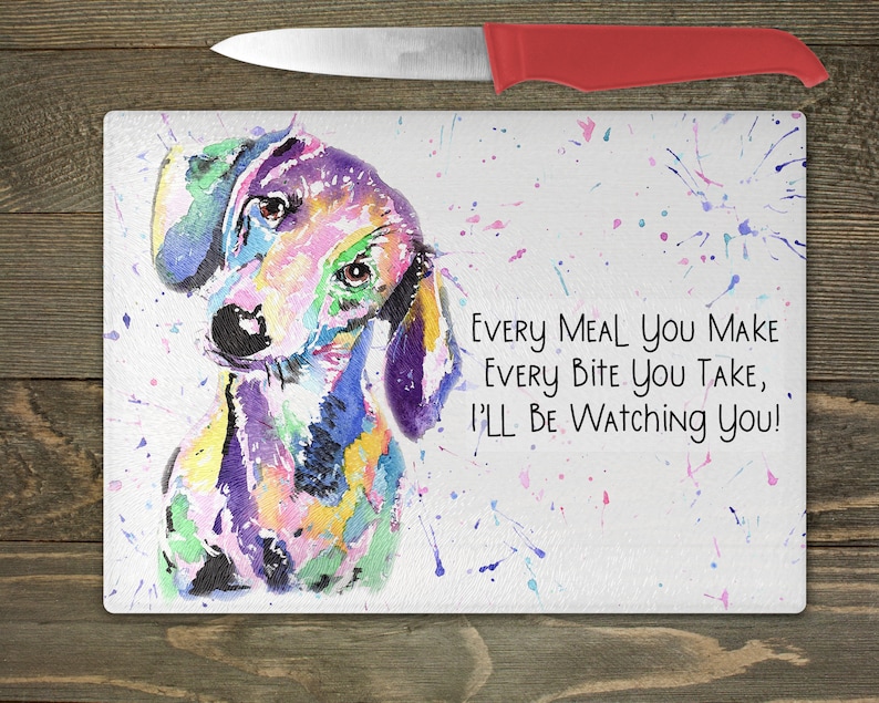 May include: A colorful watercolor painting of a dachshund dog on a white cutting board with the text "Every meal you make every bite you take, I'll be watching you!"