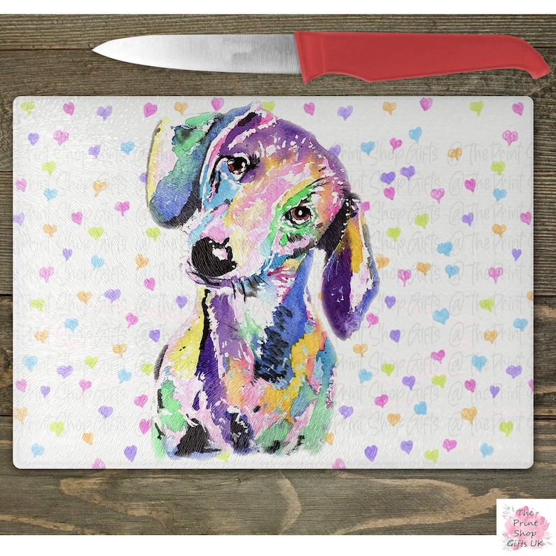 May include: A colorful watercolor painting of a dachshund dog on a white background with a pattern of small hearts in various colors. The dog is looking to the left and has a purple nose and ears.