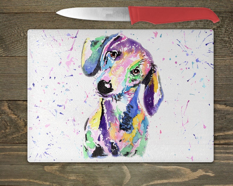 May include: A colorful watercolor painting of a dachshund dog on a white background with colorful paint splatters. The dog is looking to the left of the image.