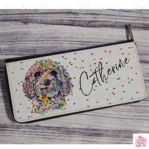 May include: A white zippered wallet with a colorful watercolor painting of a dog on the front. The wallet has a white background with small, colorful hearts scattered across the surface. The name "Catherine" is written in black cursive on the right side of the wallet.