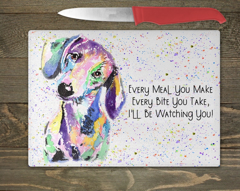 May include: A colorful watercolor painting of a dachshund dog on a white background with a splatter pattern. The text reads "Every meal you make every bite you take, I'll be watching you!"