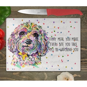 May include: A white glass cutting board with a colorful painting of a dog's face. The dog has a yellow flower on its collar. The text "EVERY MEAL YOU MAKE. EVERY BITE YOU TAKE. I'LL BE WATCHING YOU" is printed on the board.