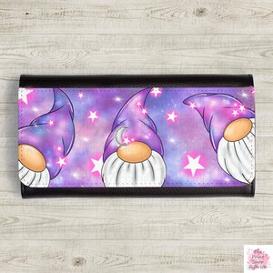 Op de afbeelding: Een zwarte leren portemonnee met een paarse en roze galaxy print met drie gnomes die paarse hoeden dragen met een halve maan en sterren.