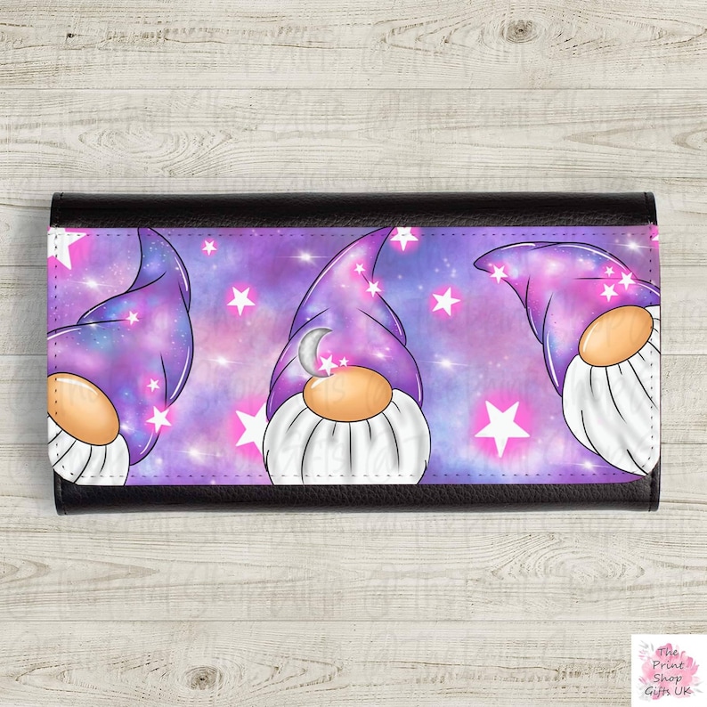 Op de afbeelding: Een zwarte leren portemonnee met een paarse en roze galaxy print met drie gnomes die paarse hoeden dragen met een halve maan en sterren.