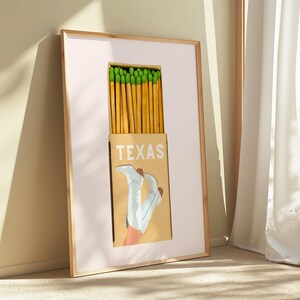 Könnte beinhalten: Ein gerahmter Kunstdruck mit einer Schachtel Streichhölzer mit grünen Köpfen und dem Wort "TEXAS". Die Box-Illustration zeigt weiße Cowboy-Stiefel. Das Kunstwerk ist vor einem weißen Hintergrund in einem goldenen Rahmen.