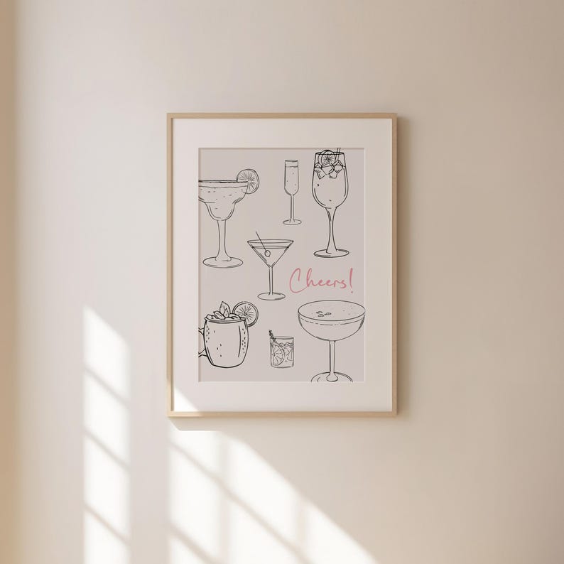 K&ouml;nnte beinhalten: Ein gerahmter Druck mit hellgrauem Hintergrund, der eine Sammlung von schwarzen Strichzeichnungen verschiedener Cocktails zeigt. Der Text "Cheers!" ist in rosa Kursivschrift geschrieben.