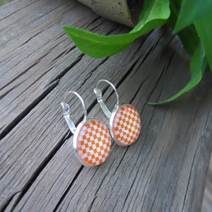 May include: A pair of silver hoop earrings with orange and white checkered round glass cabochons.