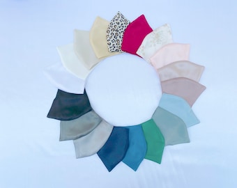 Puede incluir: Una disposición circular de diecisiete mascarillas faciales en varios colores y estampados, incluyendo blanco, crema, beige, estampado de leopardo, magenta, estampado floral, rosa pálido, topo, azul claro, verde salvia, verde bosque, azul verdoso, marino y gris oscuro.