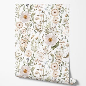 May include: A roll of wallpaper featuring a watercolor floral pattern. The design includes large white daisies with yellow centers, along with smaller flowers, green leaves, and other botanical elements in shades of beige and brown against a white background.