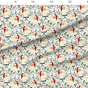 May include: A white fabric with a repeating pattern of Santa Claus faces surrounded by green leaves and red berries. The background is white.