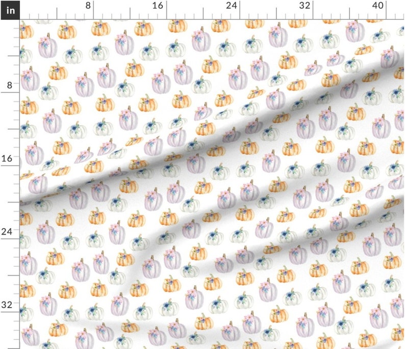 K&ouml;nnte beinhalten: Ein wei&szlig;er Stoff mit einem sich wiederholenden Muster aus Aquarell-K&uuml;rbissen in Orange-, Helllila- und Wei&szlig;t&ouml;nen, die jeweils mit kleinen blauen und rosa Blumenakzenten verziert sind, neben einem Lineal bis 100 cm.