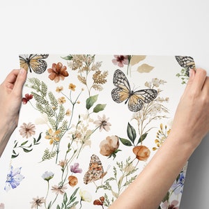 K&ouml;nnte beinhalten: Ein wei&szlig;er Hintergrund mit einem sich wiederholenden Muster aus Aquarell-Schmetterlingen und Blumen in Braun-, Gelb-, Gr&uuml;n- und Blaut&ouml;nen.