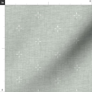 May include: Light gray fabric with a subtle texture and a repeating pattern of small white cross shapes. The fabric appears to be a woven material, suitable for various crafting or sewing projects. The image shows a section of the fabric, approximately 8 inches by 8 inches.